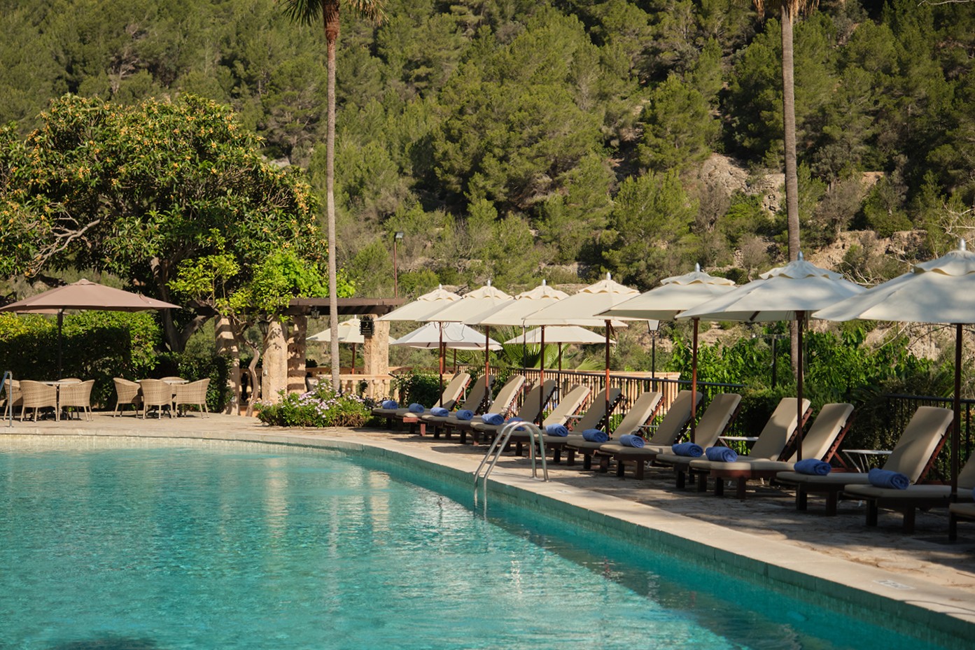 A scenic pool area bordered by lounge chairs and umbrellas, with impressive mountains in the distance, situated in Mallorca, Spain.